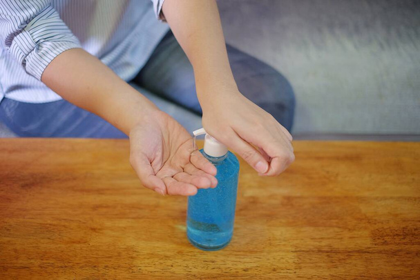 Женщина сжимает прозрачную бутылку синего антибактериального геля на деревянном столе, чтобы вымыть руки
. - Фото, изображение