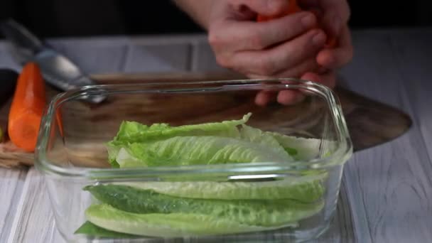 A man throws carrot slices into a transparent bowl with lettuce in slow motion. - Metraje, vídeo