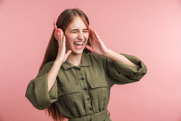 Photo of joyful caucasian woman using headphones and laughing isolated over pink background - Фото, изображение