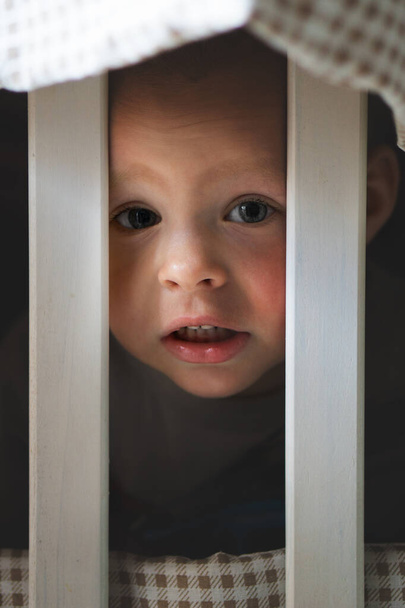 close-up portret van glimlachende schattige kleine blanke jongen spelen achter wieg hek - Foto, afbeelding