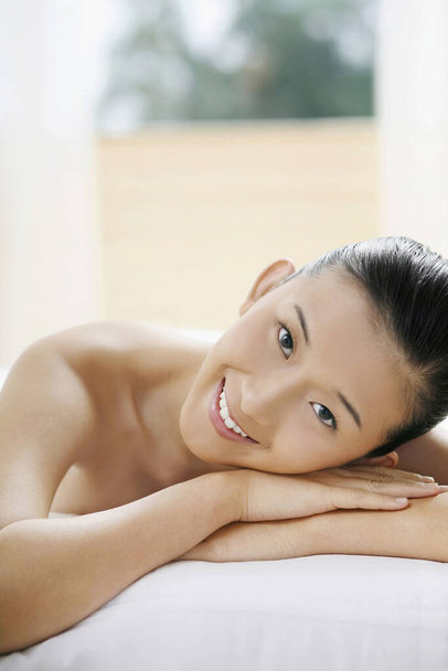 Woman lying forward on massage table, smiling - Foto, Imagem