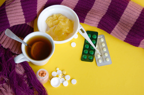 Diverse farmaceutische pillen, tabletten en capsules op gele achtergrond. Een kopje thee met citroen en een warme sjaal. Ziekte. Handhaving van de immuniteit. Seizoensziekten. Bovenaanzicht. Vlakke lay van geneesmiddelen - Foto, afbeelding