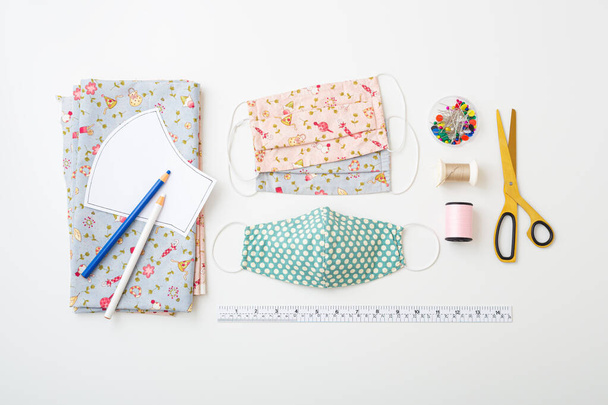 DIY Cotton face mask composition with fabric, pattern, threads, scissors, and sewing accessories on white background, flat lay - 写真・画像