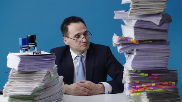 Secretario de oficina se sienta a la mesa con dos grandes pilas de papeles y toma su cabeza
 - Metraje, vídeo
