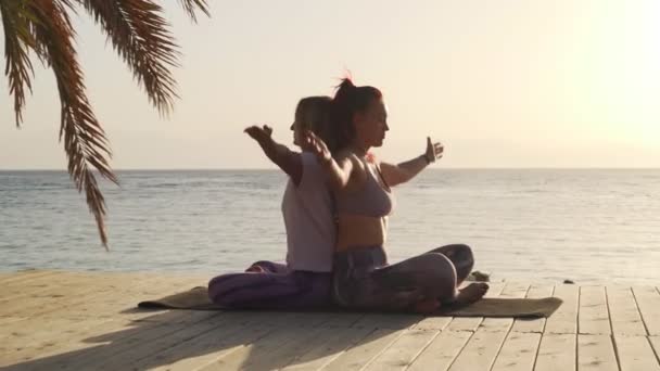 Δύο γυναίκες πρακτική κλείσιμο διαλογισμό για το σύντροφο γιόγκα στην παραλία κατά το ηλιοβασίλεμα - Πλάνα, βίντεο