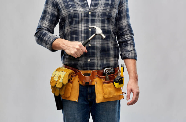 constructor masculino con martillo y herramientas de trabajo en la correa
 - Foto, imagen