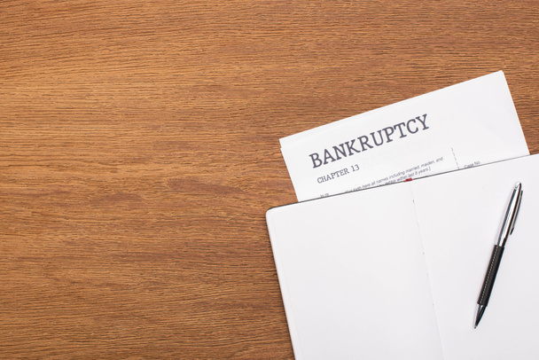 top view of bankruptcy paper and blank notebook with pen on wooden background - Photo, Image