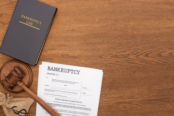 top view of bankruptcy law book, documents, money bag and gavel on wooden background - Photo, Image