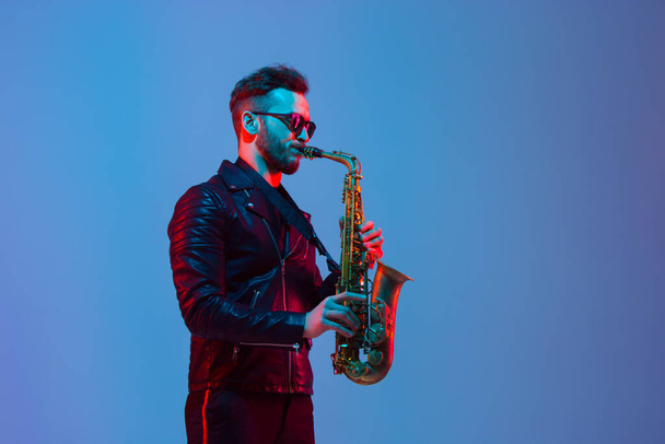 Young caucasian jazz musician playing the saxophone in neon light - Foto, Imagem