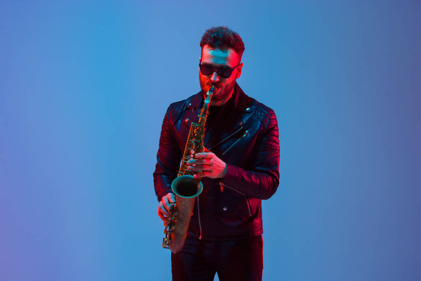 Young caucasian jazz musician playing the saxophone in neon light - Foto, afbeelding