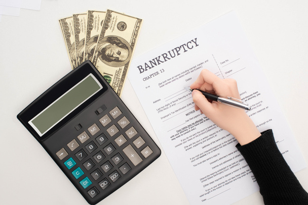 cropped view of woman filling in bankruptcy form with pen near money and calculator on white background - Fotó, kép