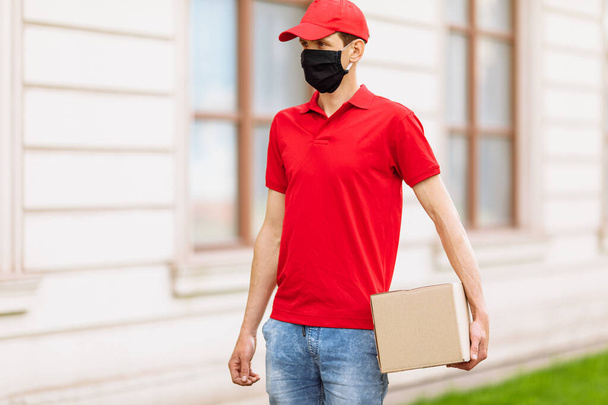 A courier in a protective medical mask with boxes in his hands delivers parcels. Service delivery in terms of quarantine, pandemic coronavirus - Фото, изображение