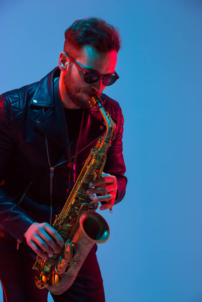 Young caucasian jazz musician playing the saxophone in neon light - Foto, Imagen