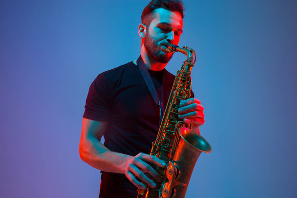 Young caucasian jazz musician playing the saxophone in neon light - Photo, image