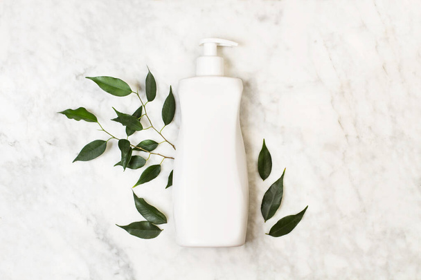 Una botella de crema corporal sobre una mesa de mármol con hojas verdes
 - Foto, imagen