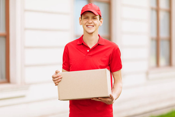 A happy uniformed Courier holds an empty cardboard box in the open air. Delivery service - Photo, image