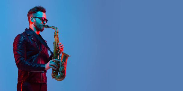 Young caucasian jazz musician playing the saxophone in neon light, flyer - 写真・画像