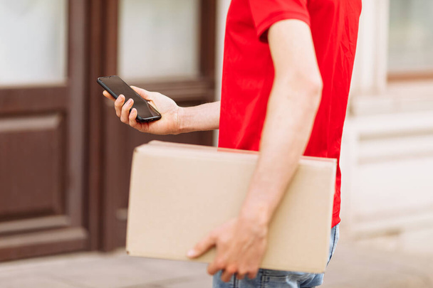 a courier with a cardboard box using a mobile phone in the open air - Photo, image