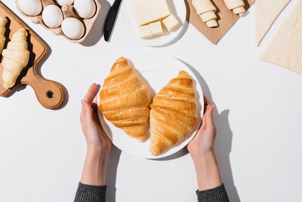 cropped view of woman holding plate with baked croissants on white background - Photo, Image