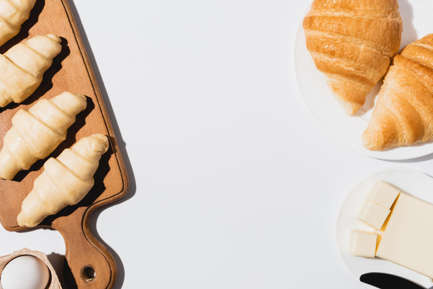 top view of tasty baked croissants on plate near raw on cutting board on white background - Φωτογραφία, εικόνα