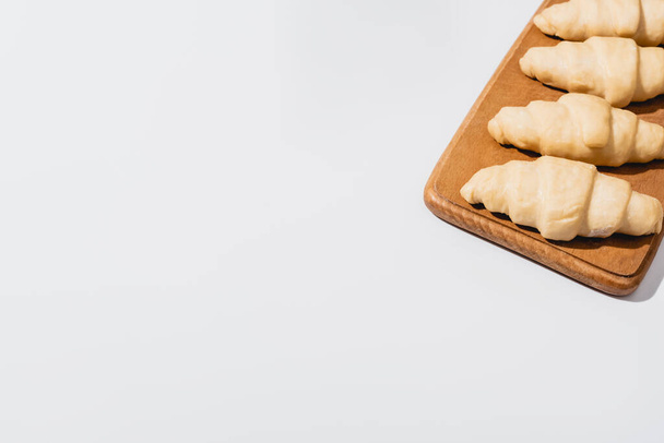 fresh raw croissants on wooden cutting board on white background - Foto, imagen