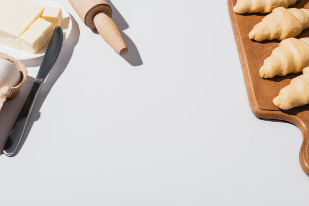 cornetti freschi su tagliere di legno vicino a coltello, mattarello, burro su sfondo bianco
 - Foto, immagini