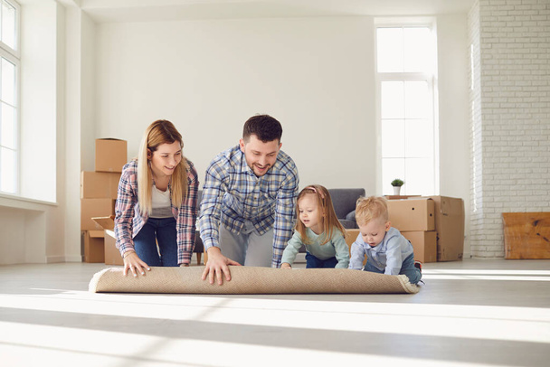 Ευτυχισμένη οικογένεια με χαλί στο πάτωμα σε ένα νέο διαμέρισμα. - Φωτογραφία, εικόνα