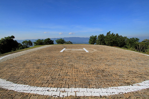 The texture of heliport on the top of high mountain with blue sky and tree background. Transportation and Pattern of tile floor - Photo, Image