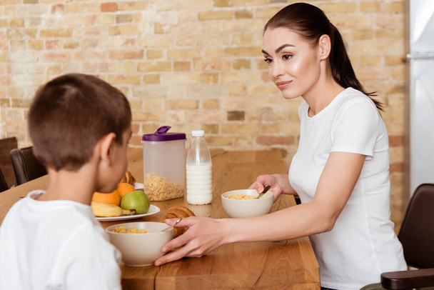 Selective focus of mother looking at son near breakfast on kitchen table  - Foto, afbeelding