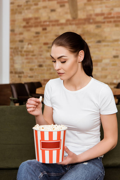 Attractive woman holding popcorn on sofa at home  - Foto, Imagem