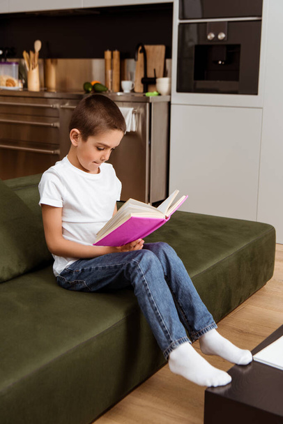 Selective focus of child reading book on couch at home  - Foto, immagini