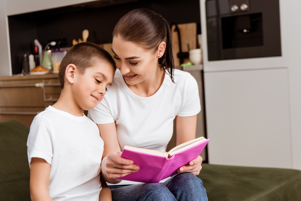 Smiling mother holding book near cute son on couch  - Φωτογραφία, εικόνα