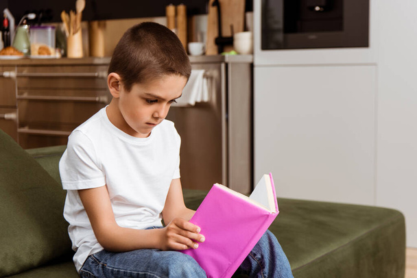 Child reading book on sofa in living room - Фото, зображення