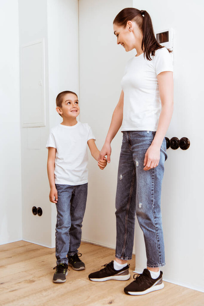 Mother and kid smiling at each other while holding hands in hallway  - Photo, Image
