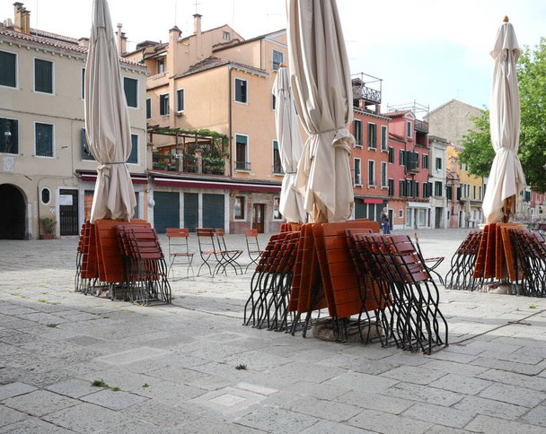 Tables and chairs of an alfresco cafe without tourists in Venice in Italy due to the Corona Virus epidemic that has blocked borders - Photo, Image