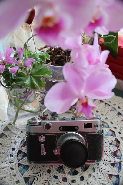 Νεκρή ζωή με μια ορχιδέα λουλούδι, ένα βάζο, κόκκινα βιβλία και μια vintage κάμερα σε ένα ντυμένο τραπέζι - Φωτογραφία, εικόνα