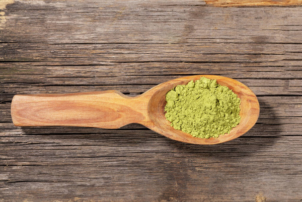 Holzlöffel mit japanischem grünen Matcha-Teepulver auf altem Holzbrett. Matcha-Tee ist ein gesundes Bio-Produkt - Quelle von Antioxidantien. Ansicht von oben, Kopierraum. - Foto, Bild