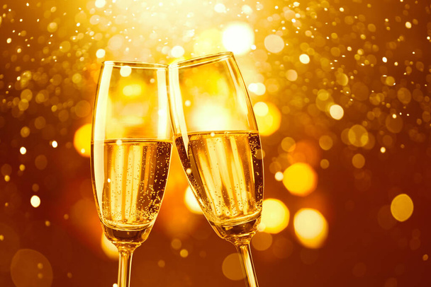 two glasses of champagne toasting against gold bokeh background - Foto, Imagem