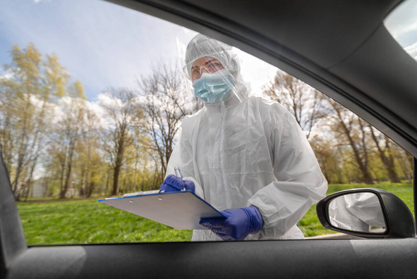 doctor in hazmat suit with clipboard at car - Photo, Image