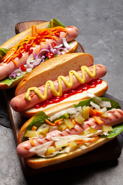 Diverse hotdog met groenten, sla en specerijen op stenen ondergrond - Foto, afbeelding