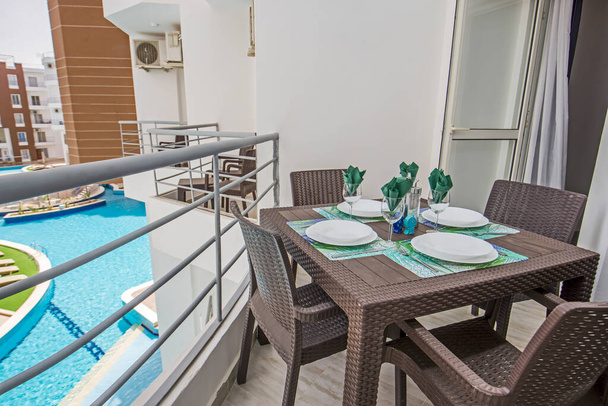 Muebles de terraza de un apartamento de lujo en complejo tropical con muebles de plástico y vista a la piscina - Foto, Imagen