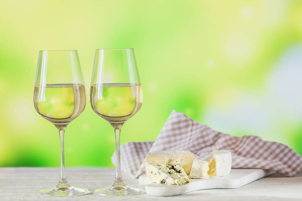 White wine served with cheese plate on light green background. Two wineglasses of vino verde. Seasonal holidays concept - Valokuva, kuva