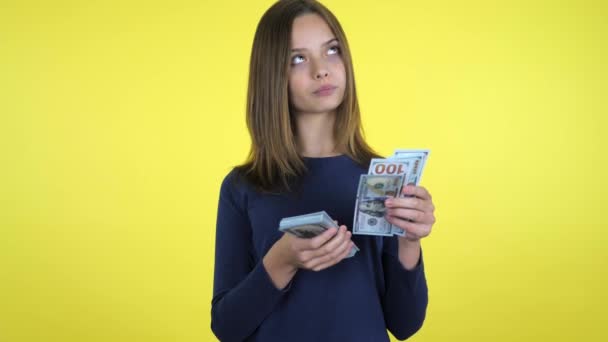 Rich girl counts money and thinks that she will buy it on yellow background - Video, Çekim