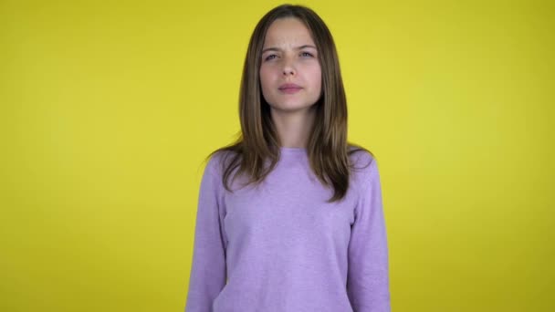 Teen girl sneezes covering her face with palms on a yellow background - Filmati, video