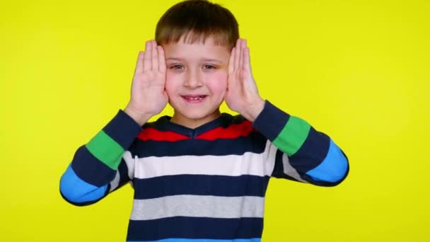 Grappig kind jongen neemt handen van zijn gezicht en glimlacht op gele achtergrond - Video