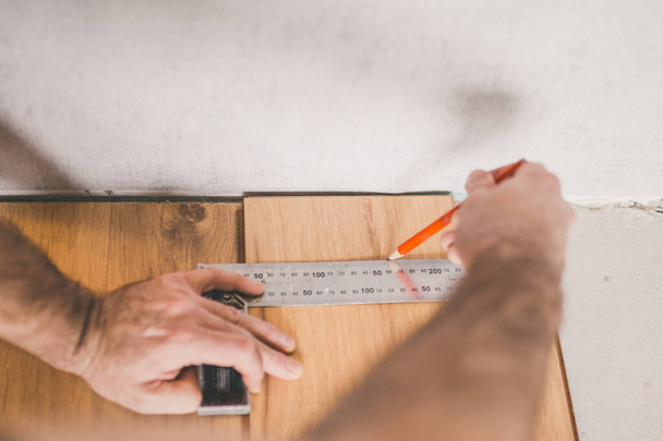 Worker measuring and marking laminate for cutting - installing floating floor - close-up on hands - home renovation concept - 写真・画像