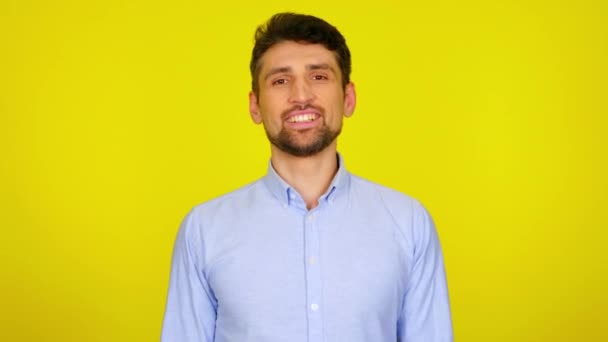 Knappe bebaarde man draait zich om naar de camera en glimlacht op een gele achtergrond - Video