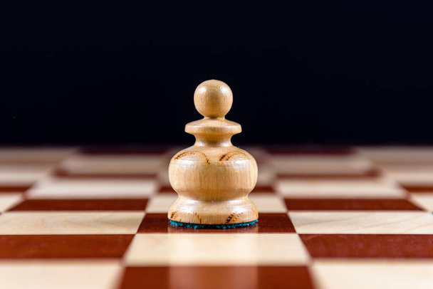 white wooden pawn on a chessboard on a black background - Foto, Imagem