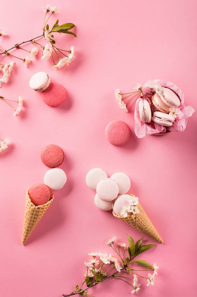 Macarrones de color rosa en caja de regalo y flores de cerezo. Macarons dulces presentes en el fondo rosa con espacio de copia. Vista superior. Concepto de vacaciones
 - Foto, Imagen