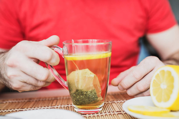 Vista de xícara de vidro de chá com hortelã na mão masculina limão, mel e geléia
 - Foto, Imagem